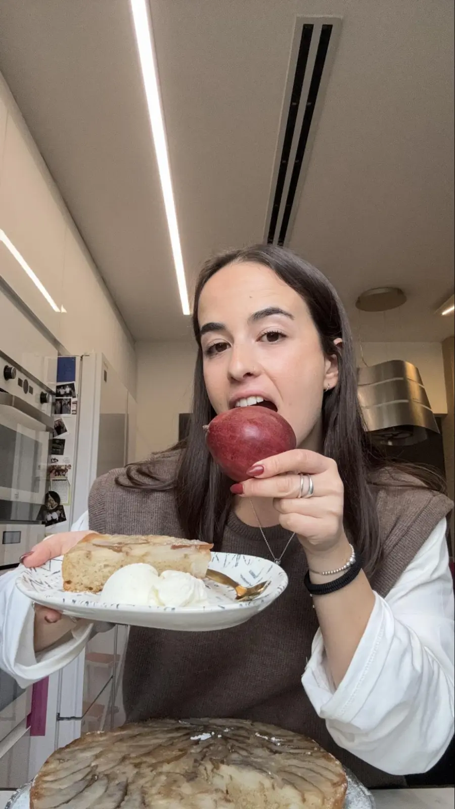 אלונה במטבח מחזיקה צלחת עוגה עם גלידה ואגס אדום